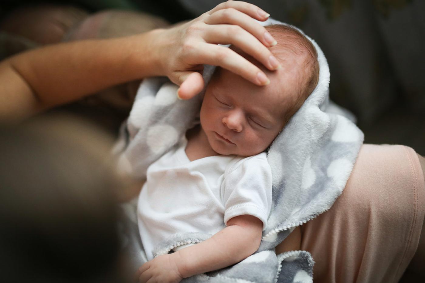 A mom gently supports a sleeping infant during a calming therapeutic session focused on nurturing comfort, regulation, and postpartum healing.